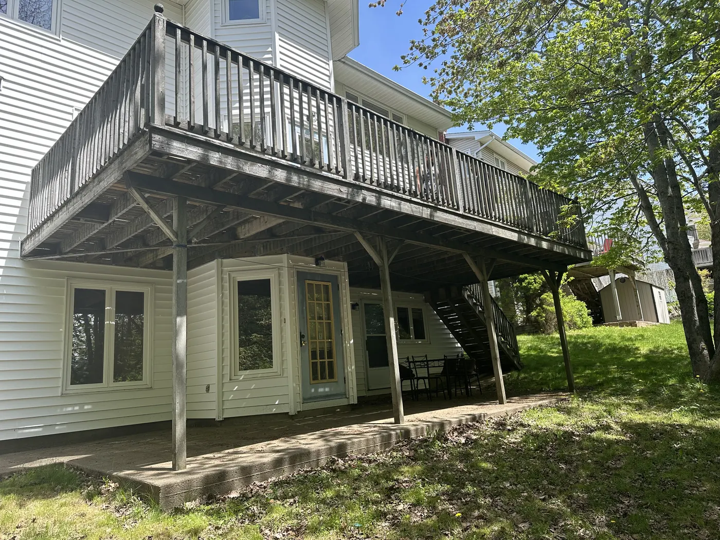 Weathered elevated deck underside with grey railings on a white-sided house, before rebuild